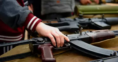 La mano de un nio toma un rifle automtico de la mesa con armas. Foto de primer