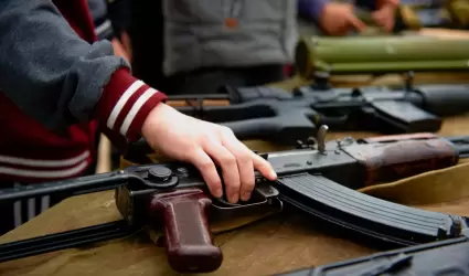 La mano de un nio toma un rifle automtico de la mesa con armas. Foto de primer